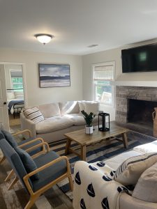 Lake-inspired living room with white and blue furniture. A painting of a beach in the back brings out the blue from the rug, blanket, pillows, and chairs.