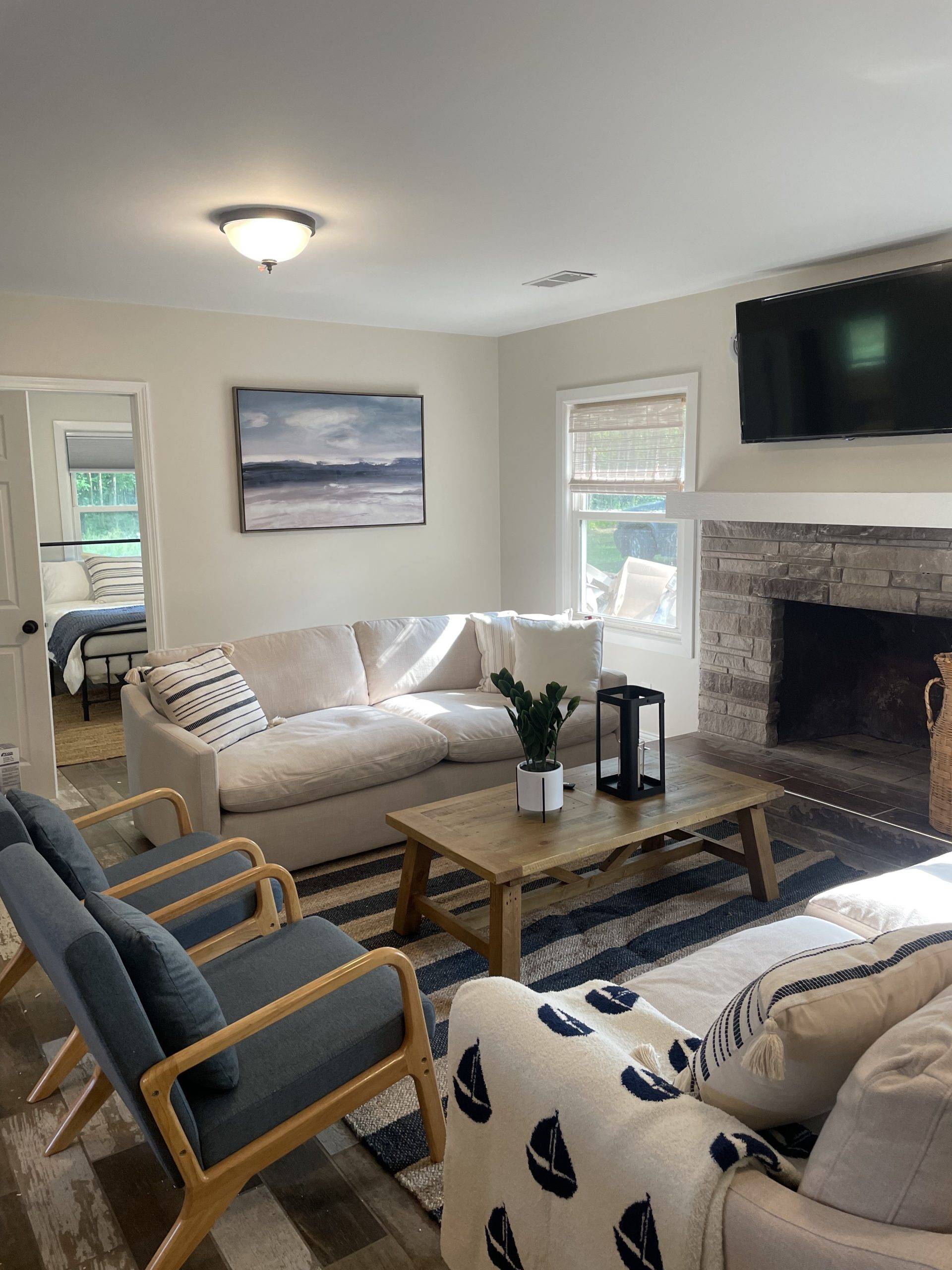 Lake-inspired living room with white and blue furniture. A painting of a beach in the back brings out the blue from the rug, blanket, pillows, and chairs.